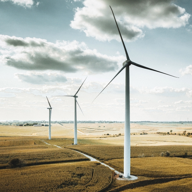 Three windmills turn above the landscape in a partly cloudy sky