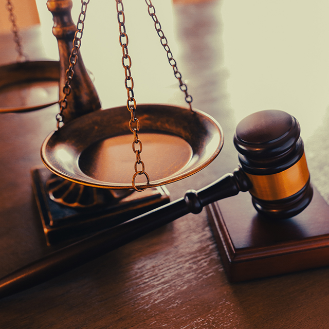 A gavel sits in front of a justice scale on a desk.