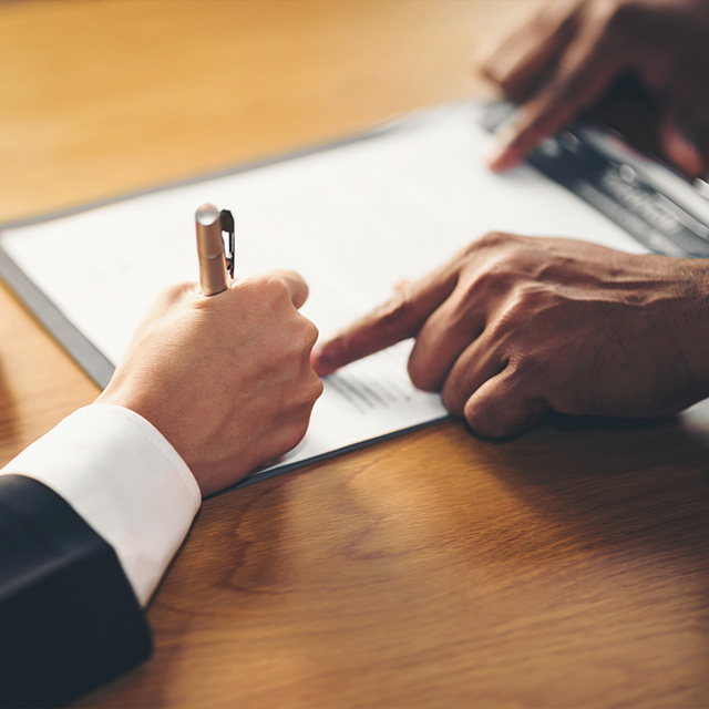 a man signing papers with another person pointing at something