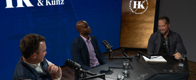 Three males sit around a table, recording a podcast.